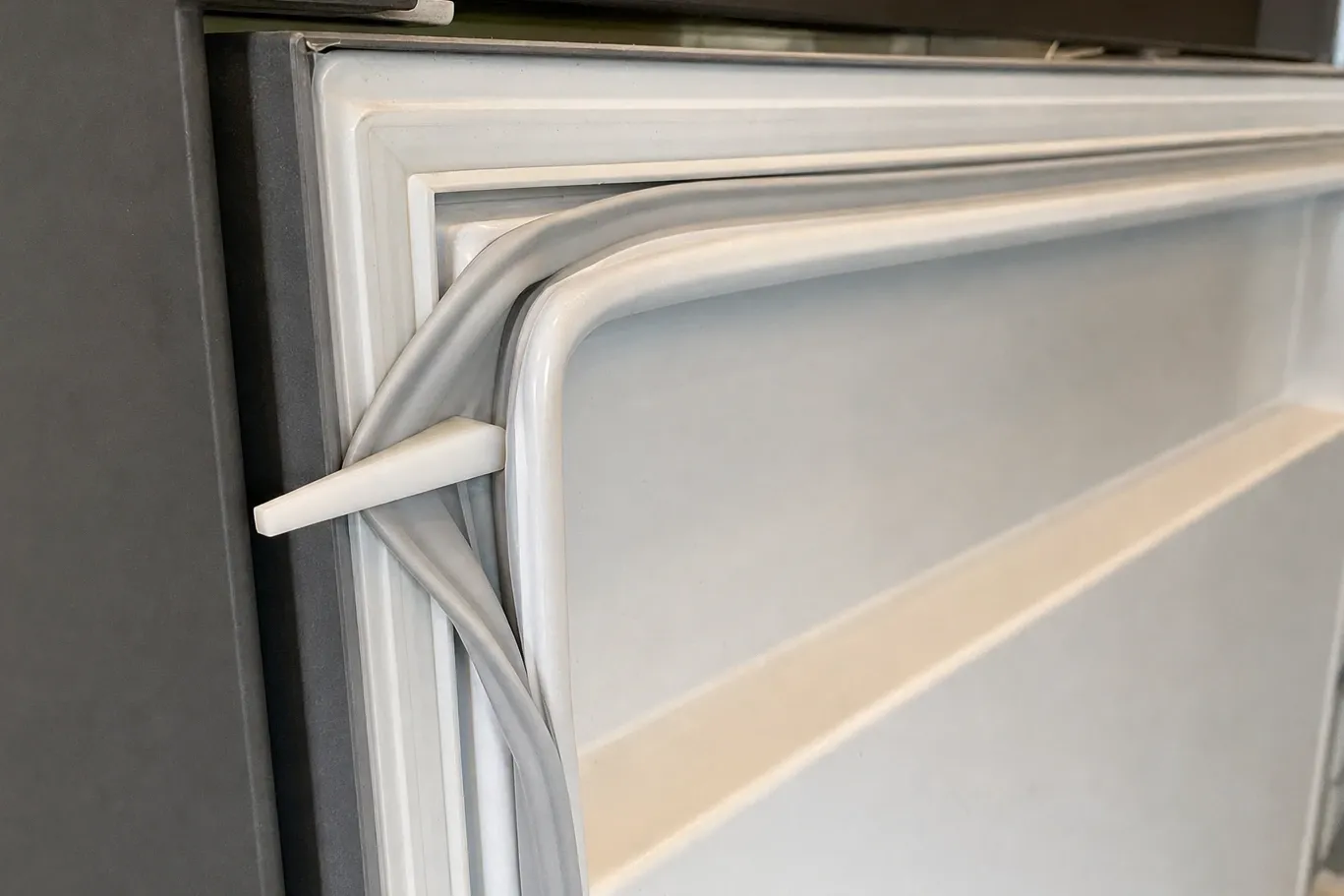 Close-up of a door gasket lifted clear of its channel at the corner of a cabinet with a plastic trim tool